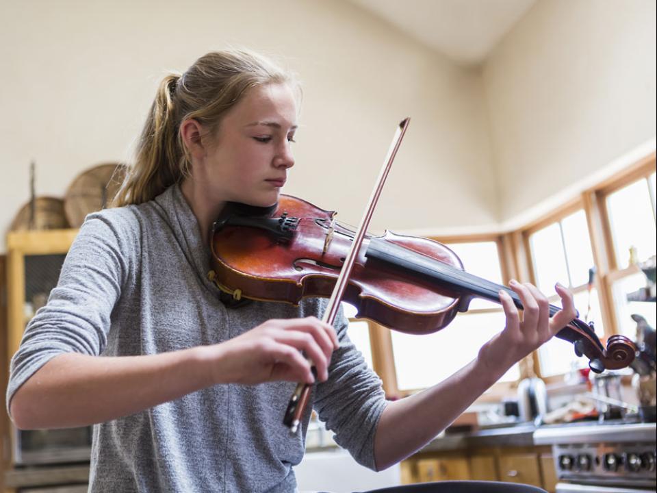 Teen playing violin at home in kitchen