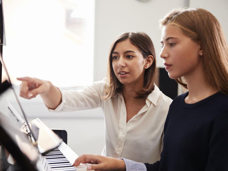 female-pupil-with-teacher-playing-piano-in-music