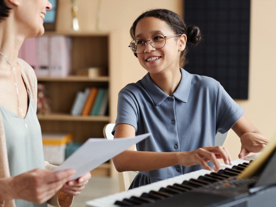 A young girl learning to play piano with her teacher